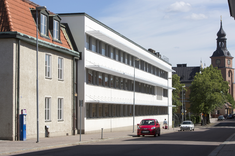 Två sammansatta byggnader samtliga i 3 våningar, den ena grå och den andra vit. 