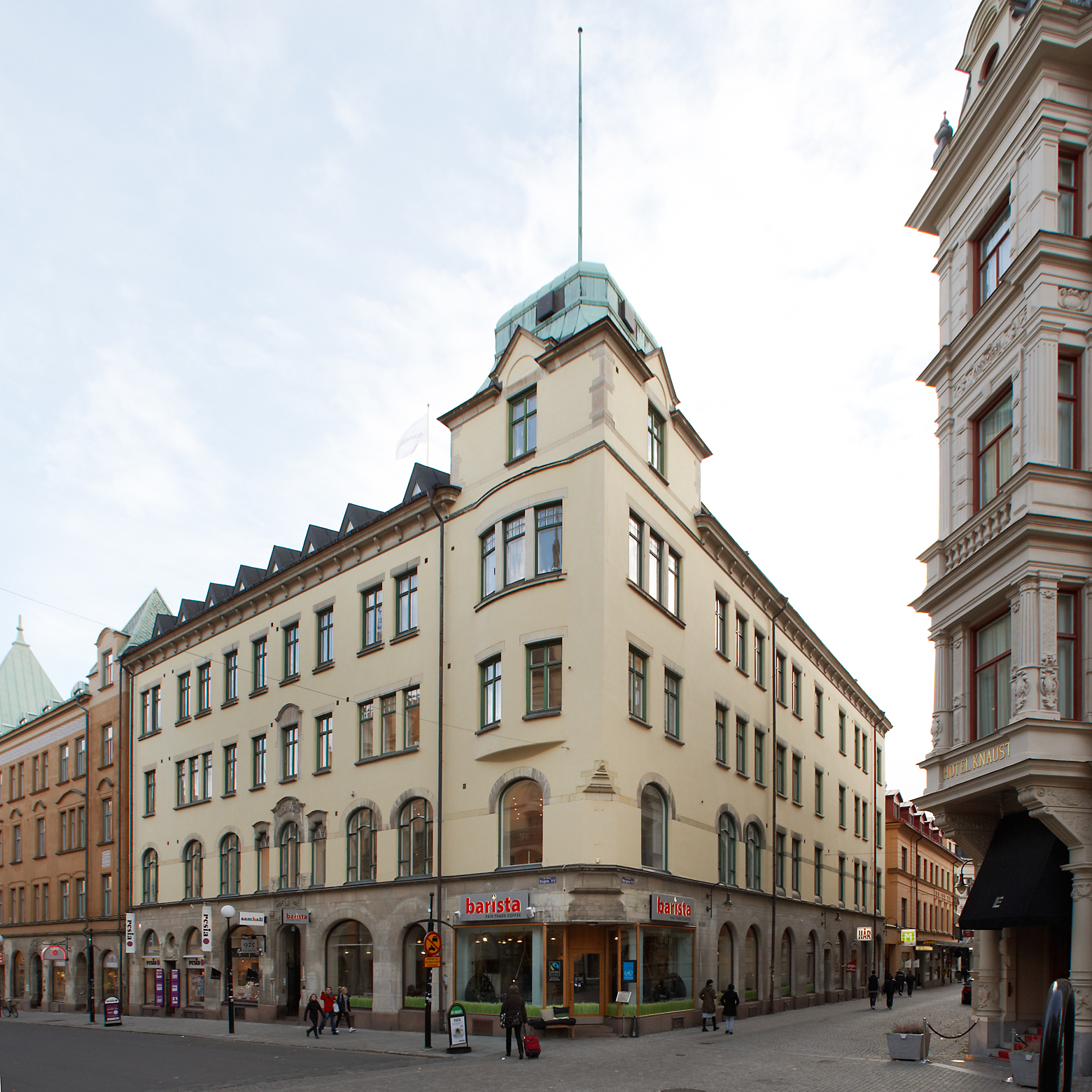 Ljusgul stenbyggnad i 5 våningar, högst upp i hörnet finns ett torn. 