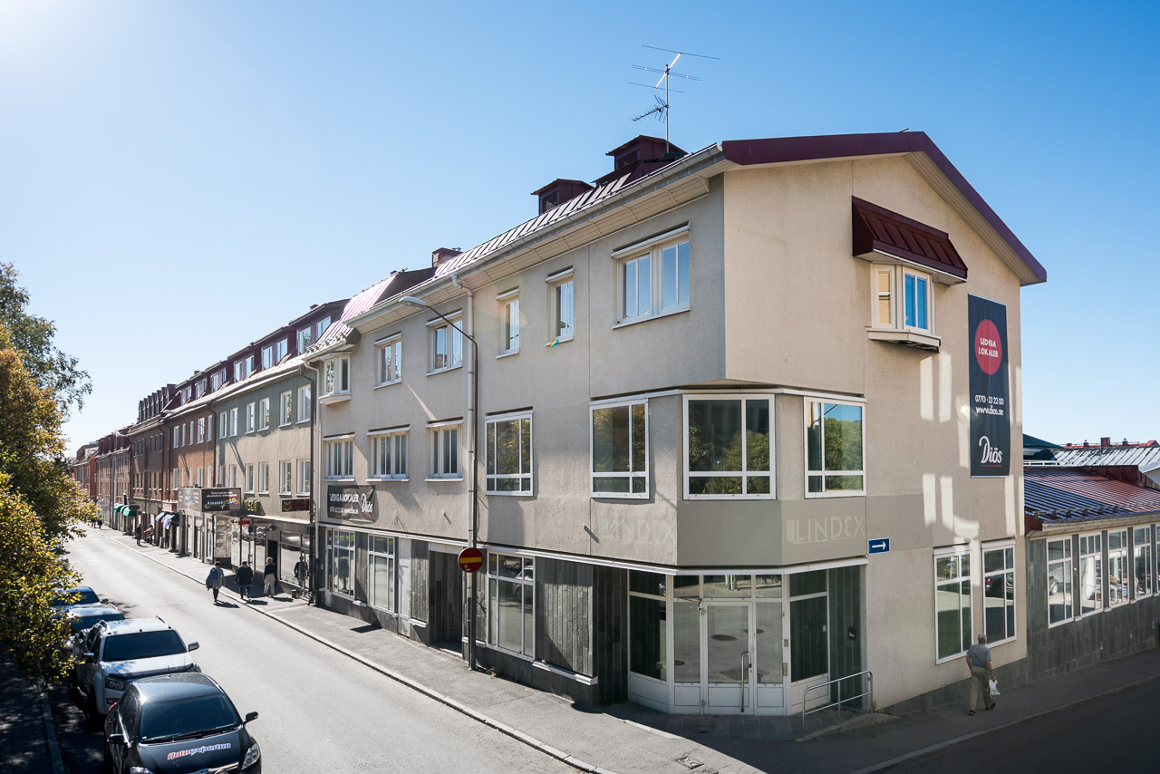 Grå byggnad i 3 våningar. Butiker och lokaler på nedersta plan. 